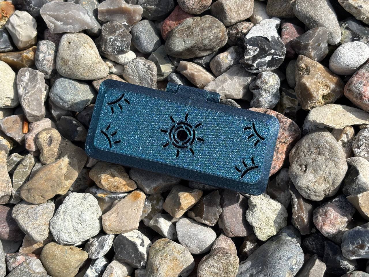 The FswStudio Reed Case for 3 Oboe Reeds is a small, dark green handmade box featuring eye and Sun designs on its lid, shown on multicolored stones—ideal for safely storing your oboe reeds.