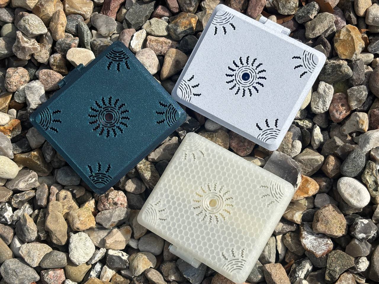 Three square FswStudio Reed Cases for 10 oboe reeds—one teal, one white, and one translucent from the Sun series—feature circular and line designs. Displayed on multicolored rocks, theyre ideal for storing oboe reeds.