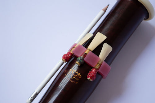 Pink silicone Bassoon Ring on a bassoon bell, holding two reeds and a pencil