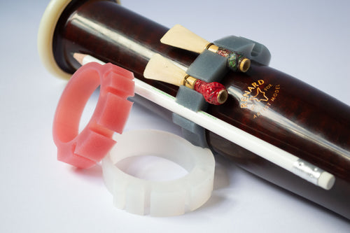 Pink and clear silicone Bassoon Rings beside a bassoon bell, with a grey ring holding two reeds and a pencil