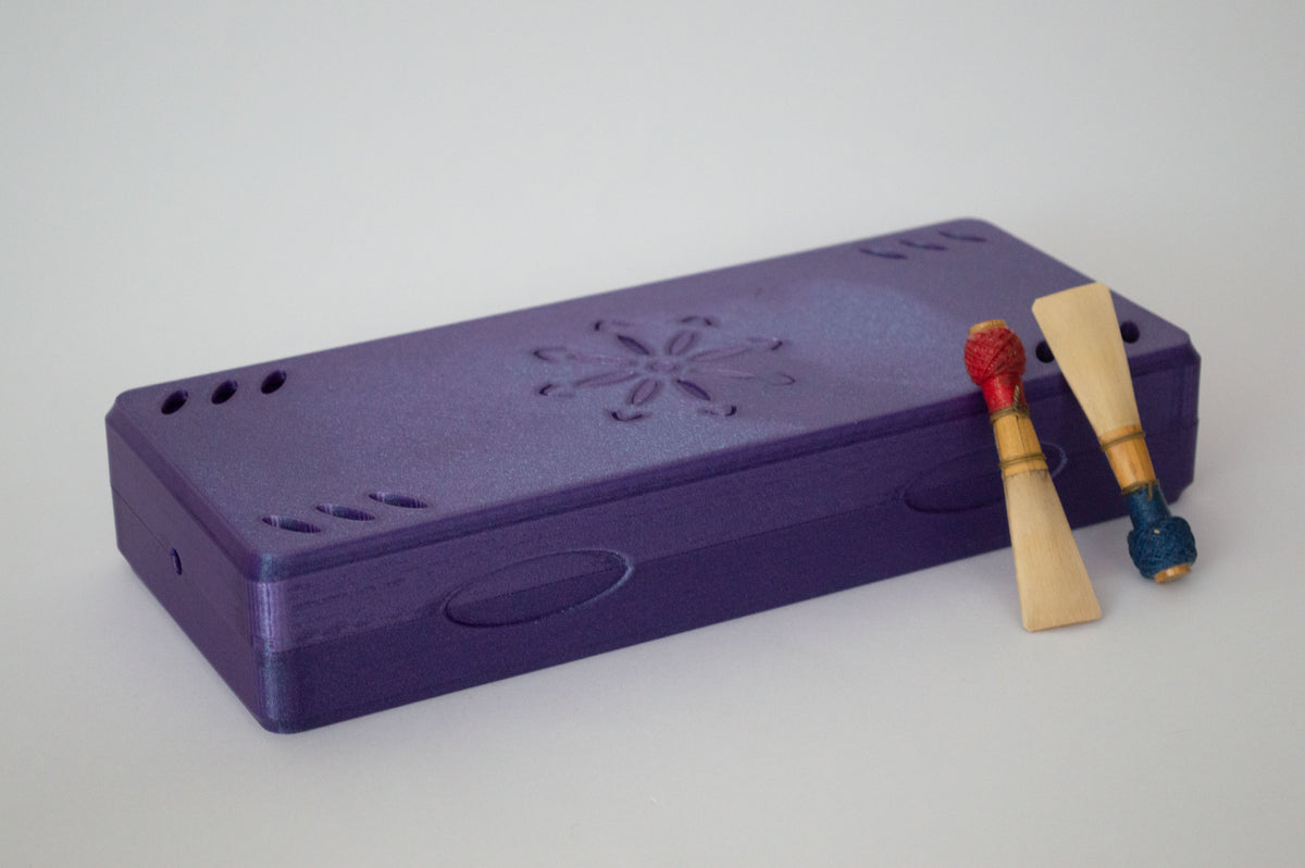 Étui à anches de basson imprimé en 3D violet, avec une gravure florale, montré avec deux anches.