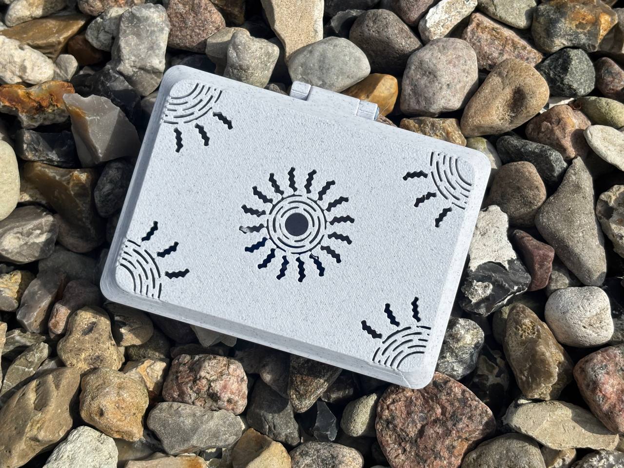 The FswStudio Reed Case for 10 English Horn Reeds from the Sun series features black sun designs on a handmade white box, shown closed and slightly off-center atop multicolored rocks.