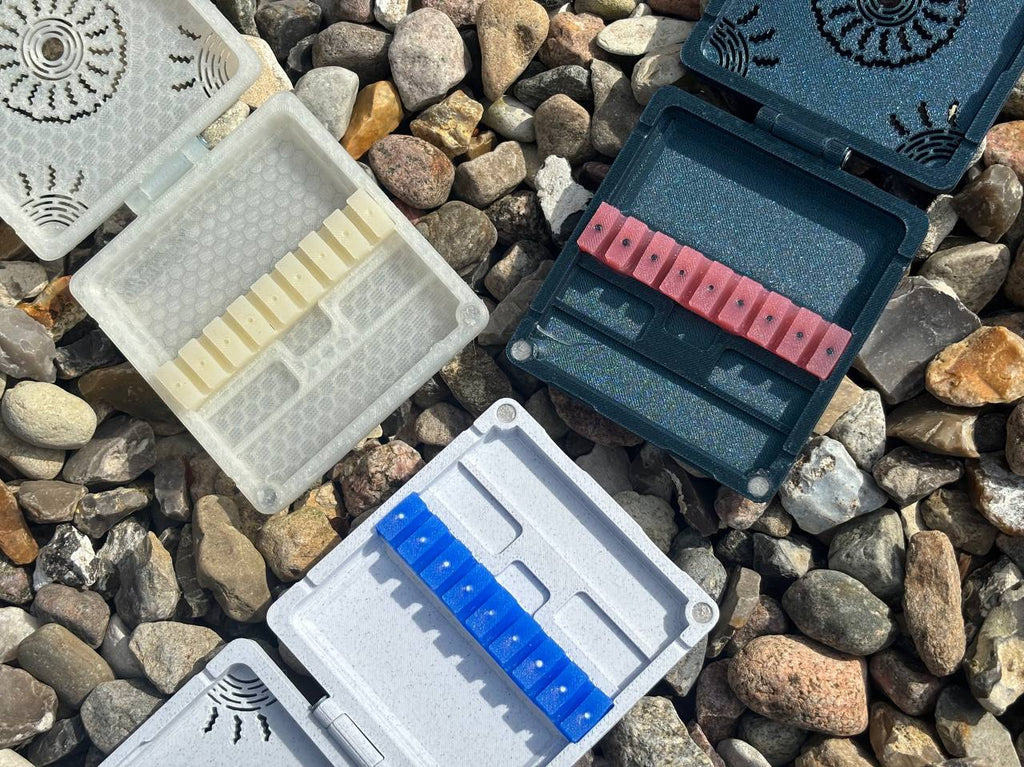FswStudios Combined Reed Case for 5 Oboe and 3 English Horn Reeds features three open handmade cases with white, red, and blue keys displayed on assorted stones outdoors—ideal for securely storing your reeds.